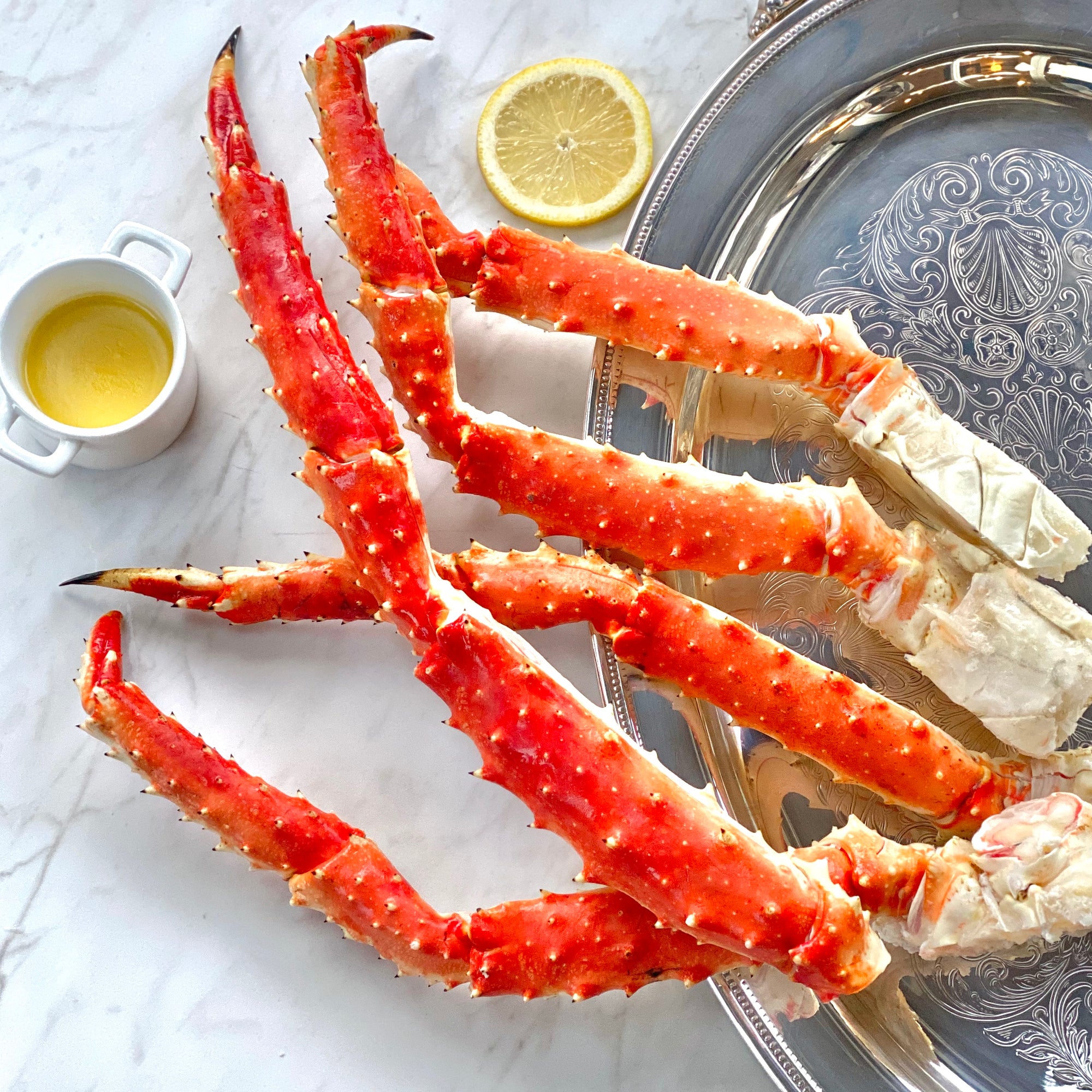A set of cooked Alaskan Red King crab legs on a plate with a slice of lemon and a small dish of butter.