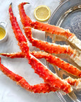 A set of cooked Alaskan Red King crab legs on a plate with a slice of lemon and a small dish of butter.