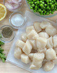 Raw wild Alaska weathervane scallops on a plate with lemon and herbs