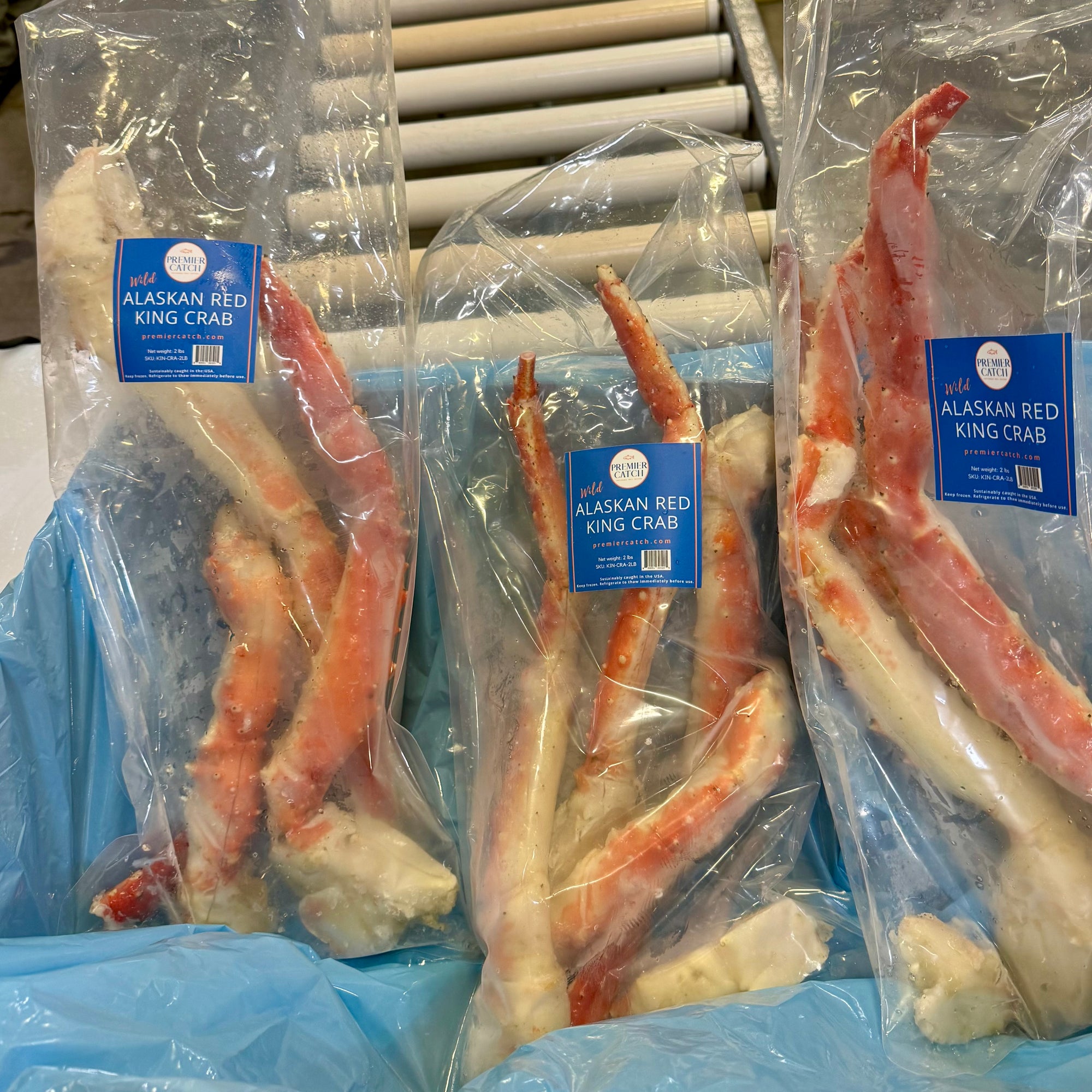 Packaged Alaskan Red King Crab legs with blue labels on a refrigerated shelf.