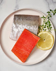 Wild Alaskan sockeye salmon portions on a plate with lemon and herbs.