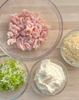 Wild oregon shrimp in a bowl with parm cheese, green onions and may in small bowls on top of a cutting board