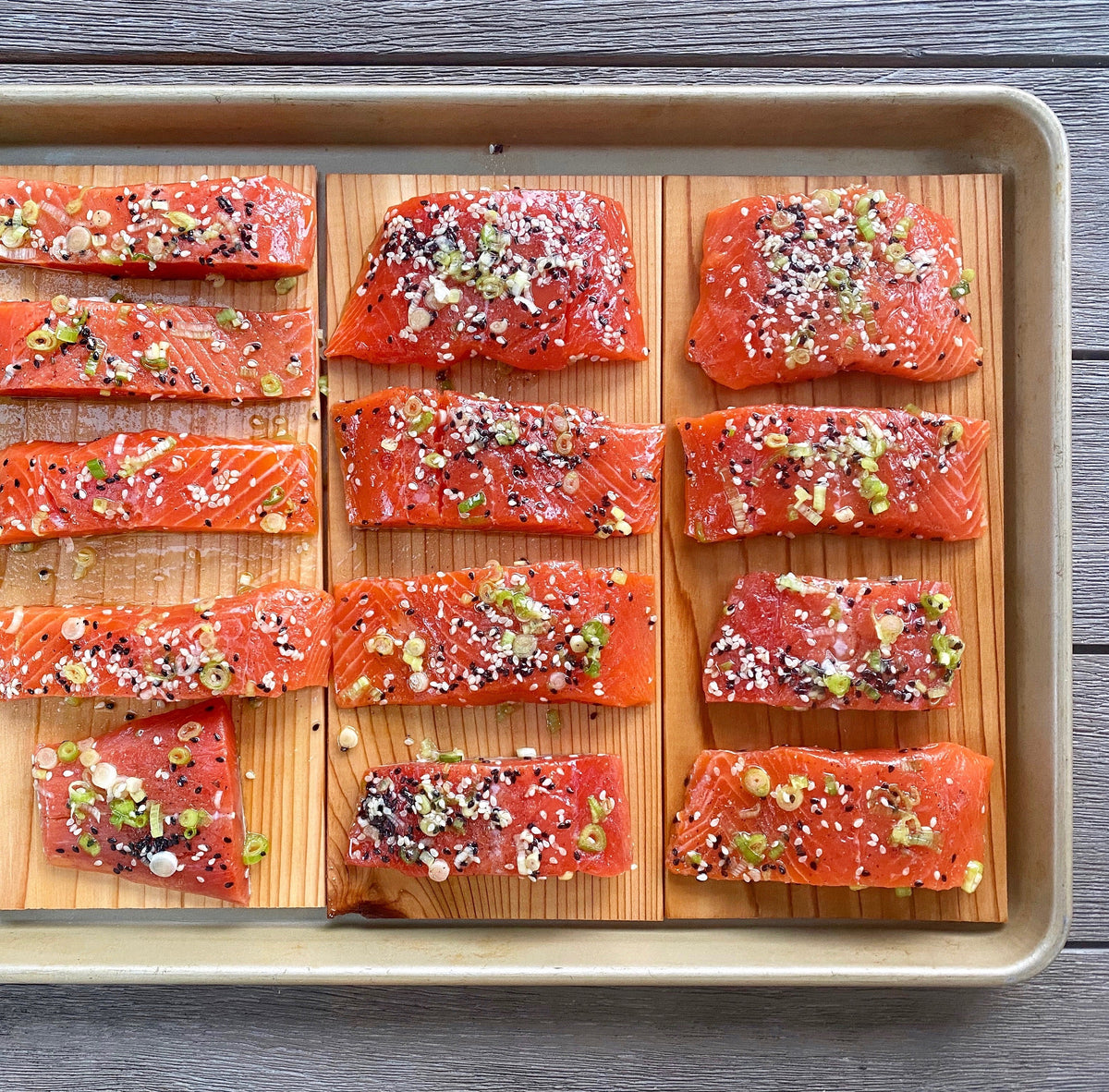 Seasoned salmon portions arranged on cedar planks in a sheet pan