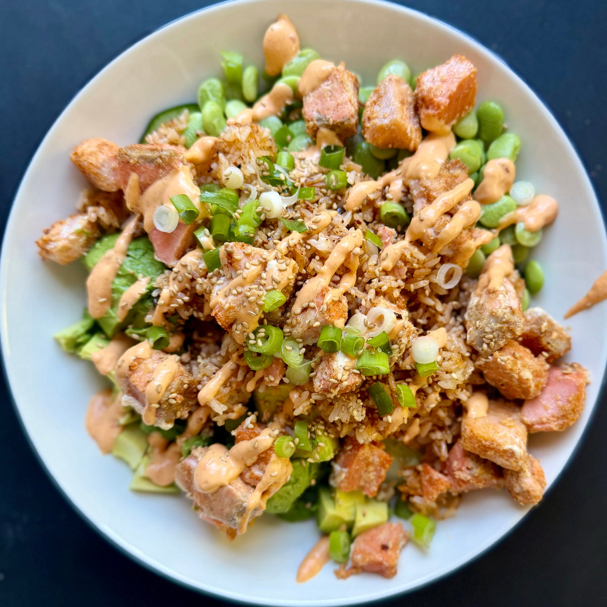 Crispy rice salmon cucumber and edamame in a bowl with sauce and green onions