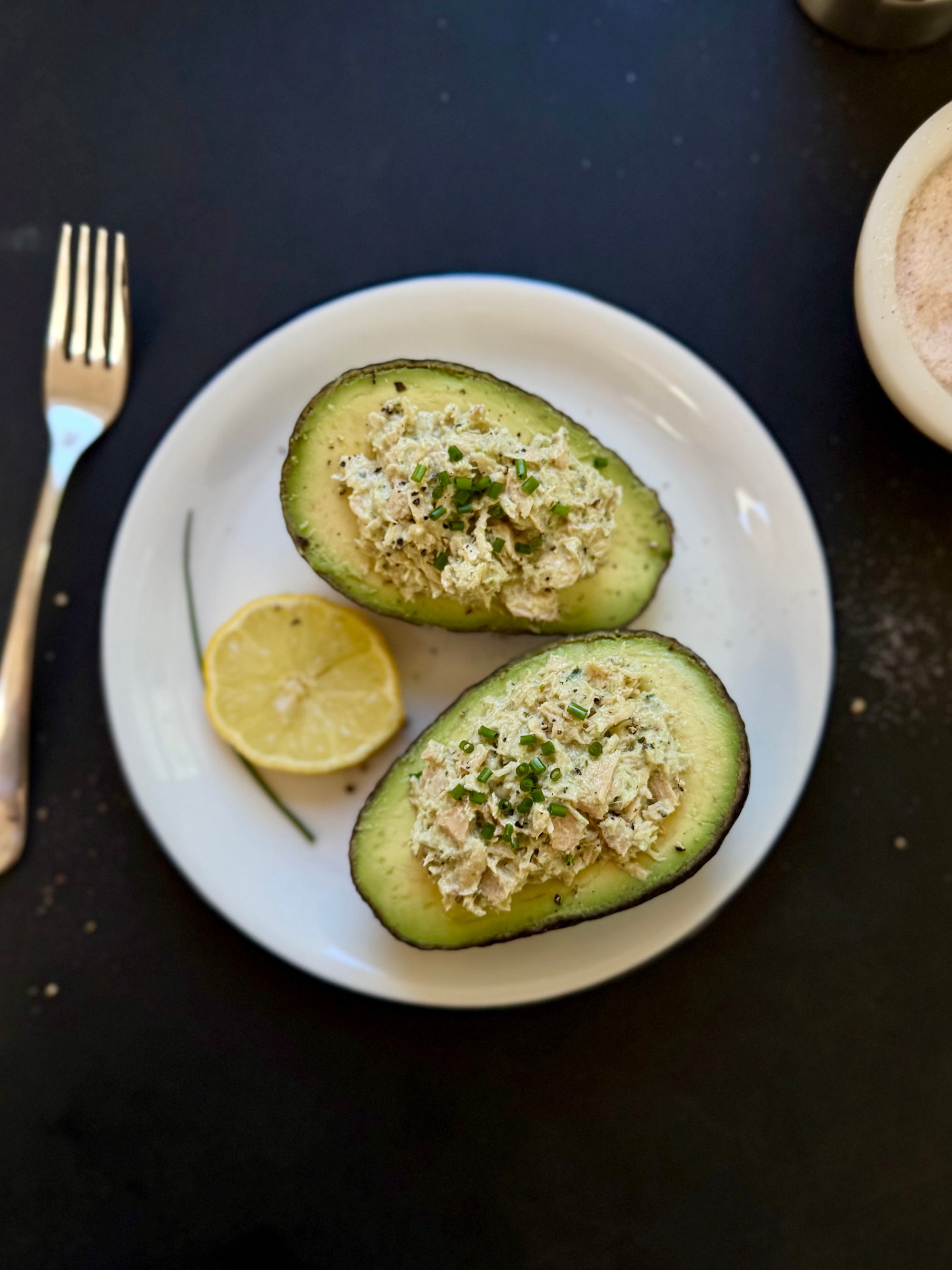 Garlic albacore tuna stuffed avocado halves topped with fresh chives and served with a lemon wedge.