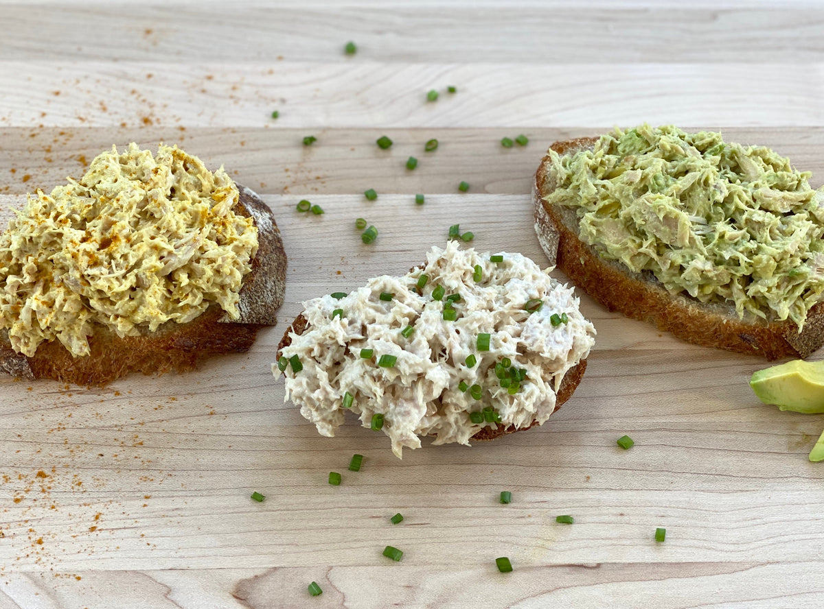 Three toasts topped with three different albacore tuna salads, scattered with chives