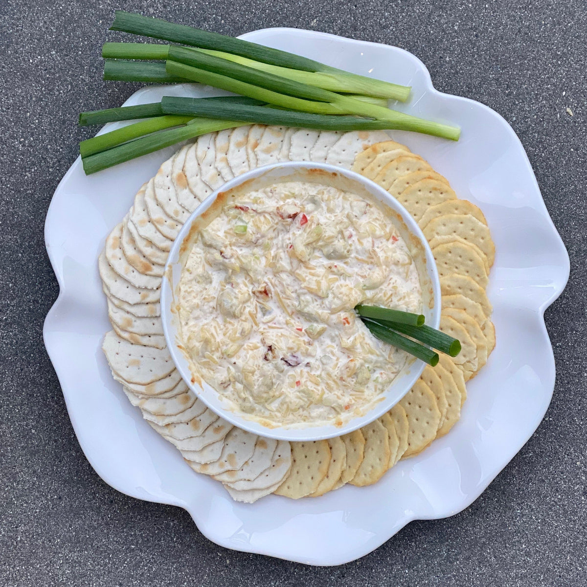 Creamy crab dip in a white bowl surrounded by round crackers and green onions