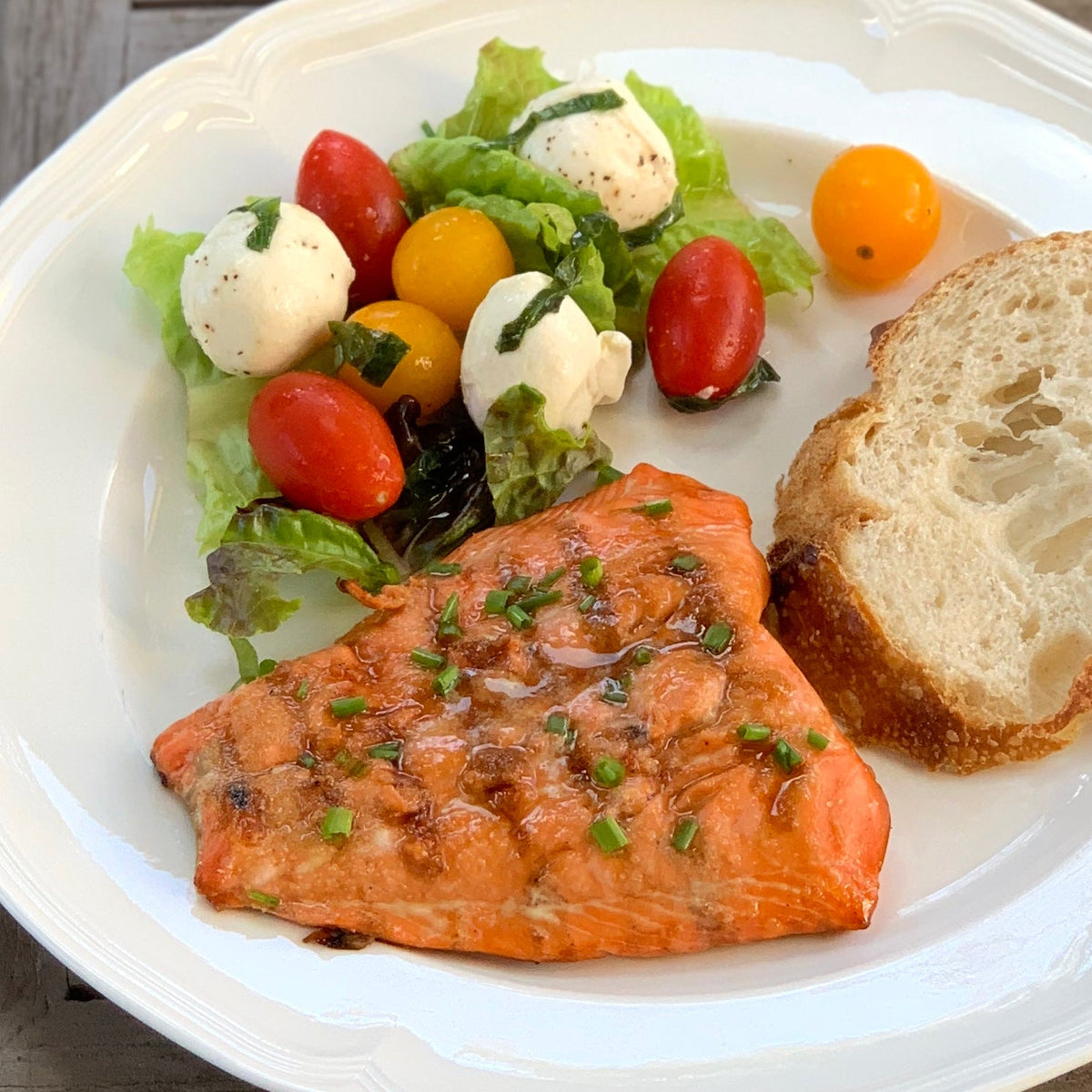 Grilled salmon fillet topped with chives, served with a caprese salad and crusty bread