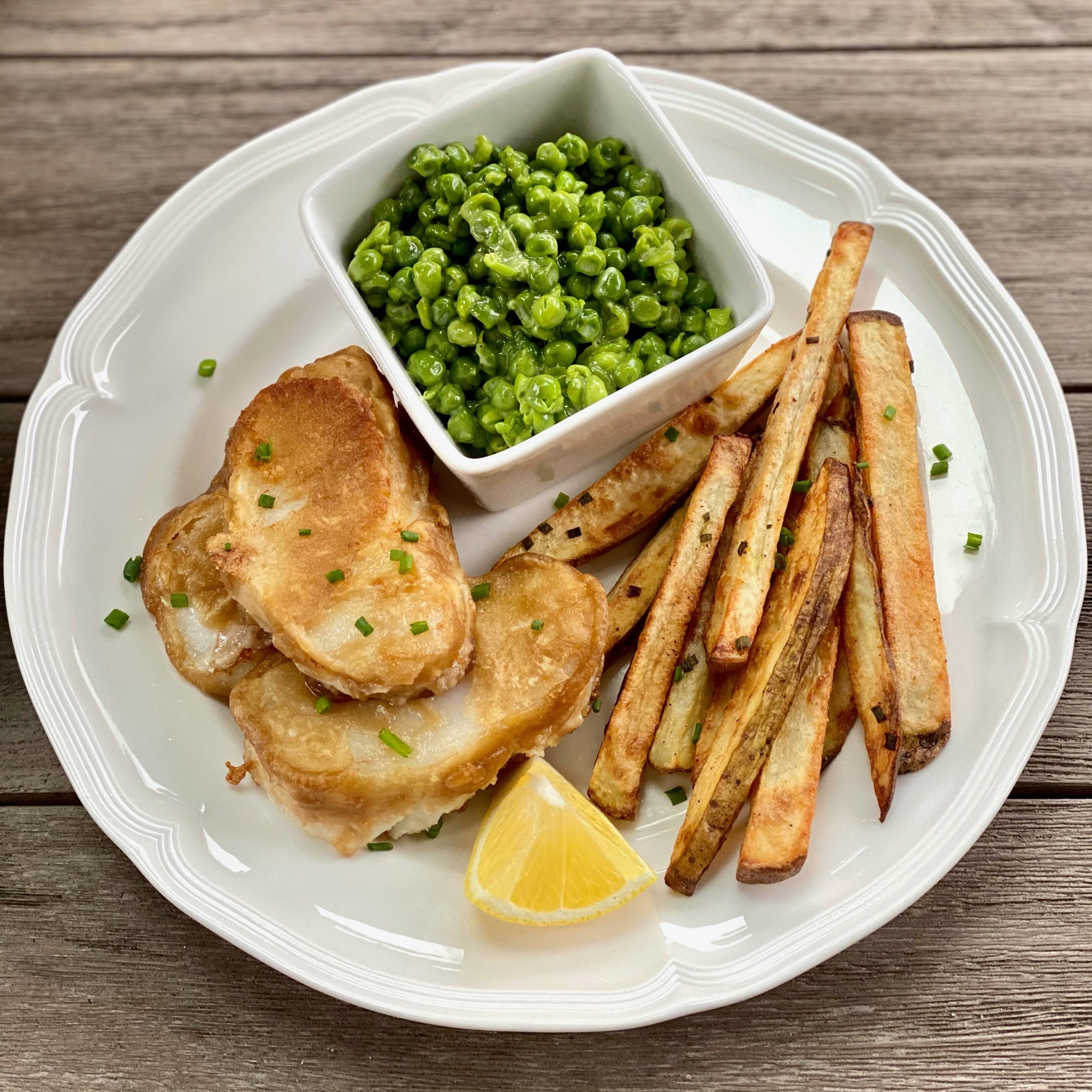 Wild Alaska cod fish and chips with crispy beer-battered cod, golden fries, and creamy mushy peas served with lemon on a white plate