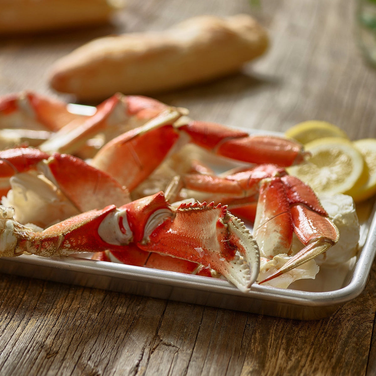 Tray of Dungeness crab legs on a wooden table with lemon wedges
