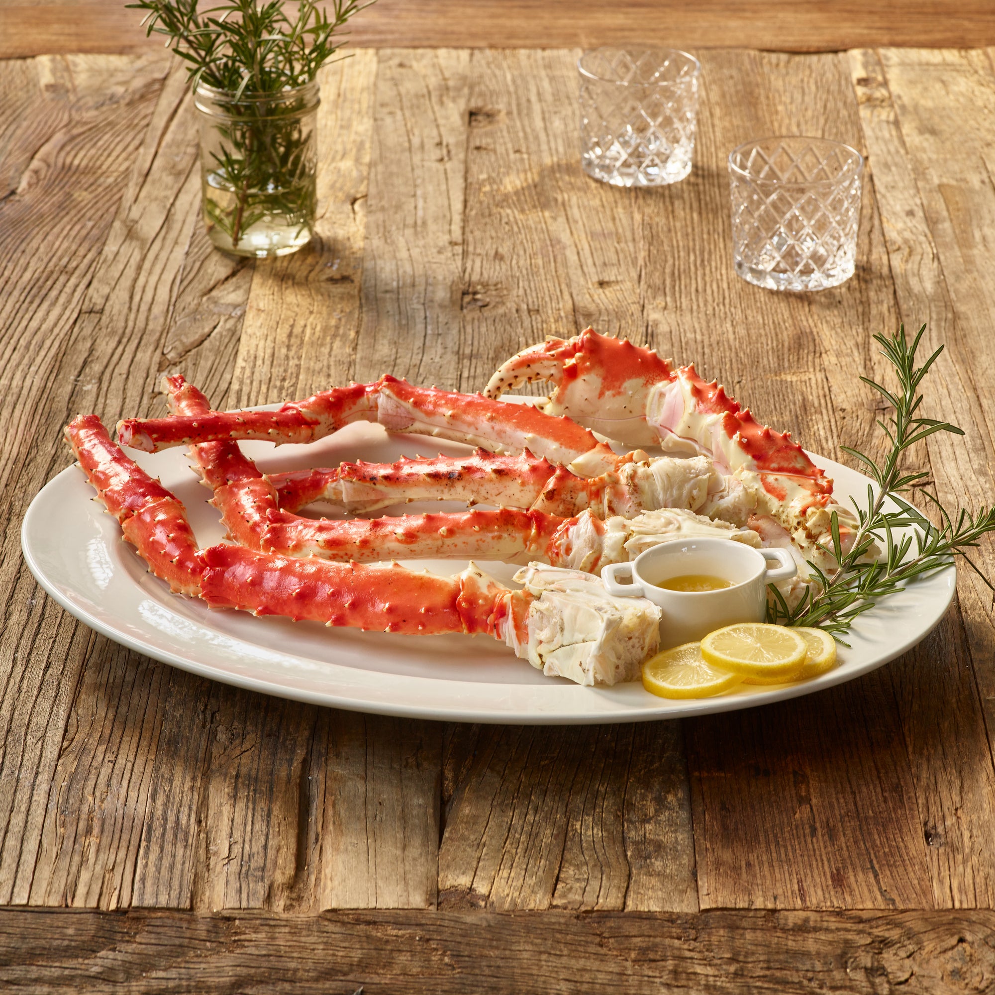 Plated red king crab legs with lemon wedges and rosemary on a wooden table