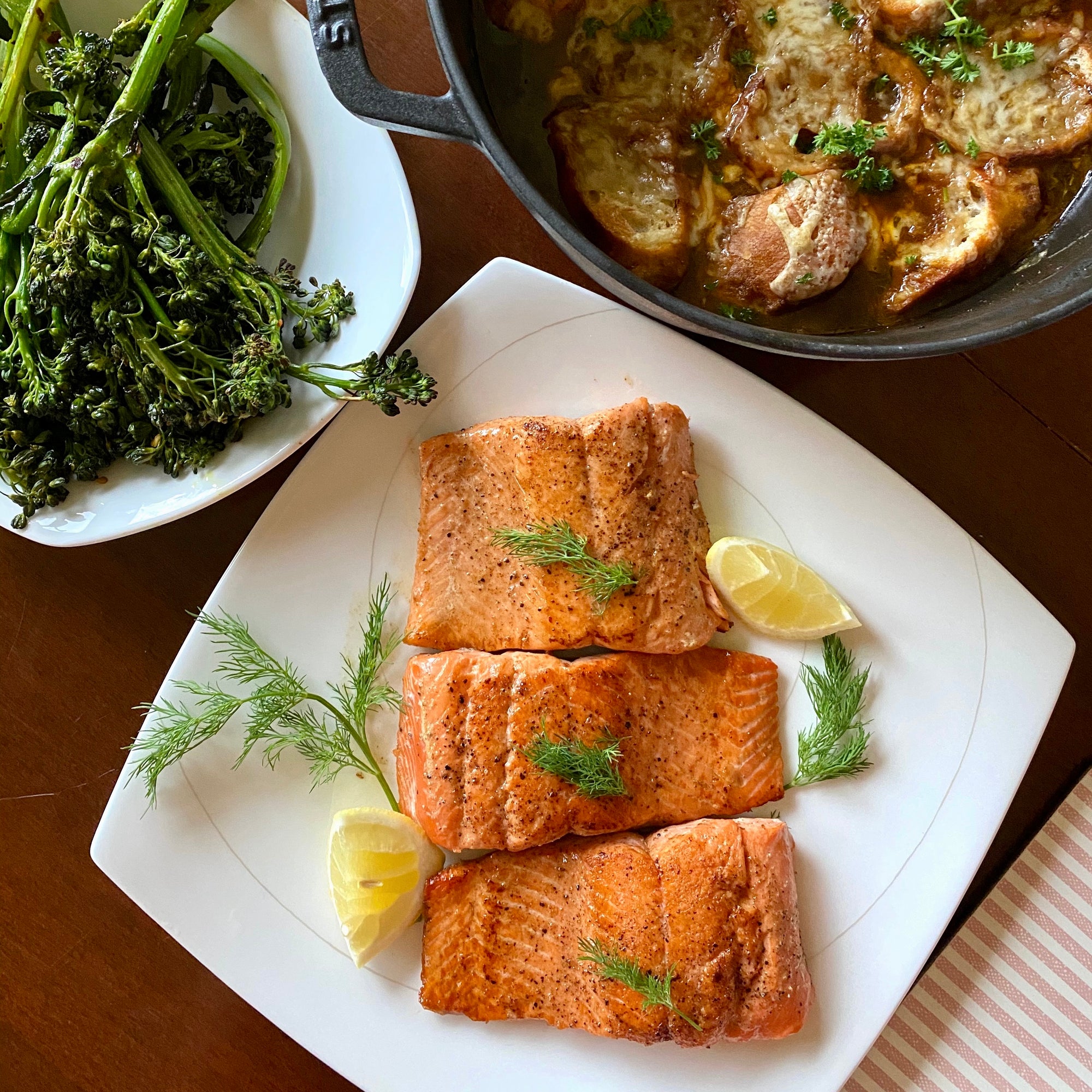 Plated salmon with lemon and dill on a white plate, accompanied by a side of greens.