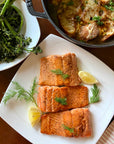 Plated salmon with lemon and dill on a white plate, accompanied by a side of greens.