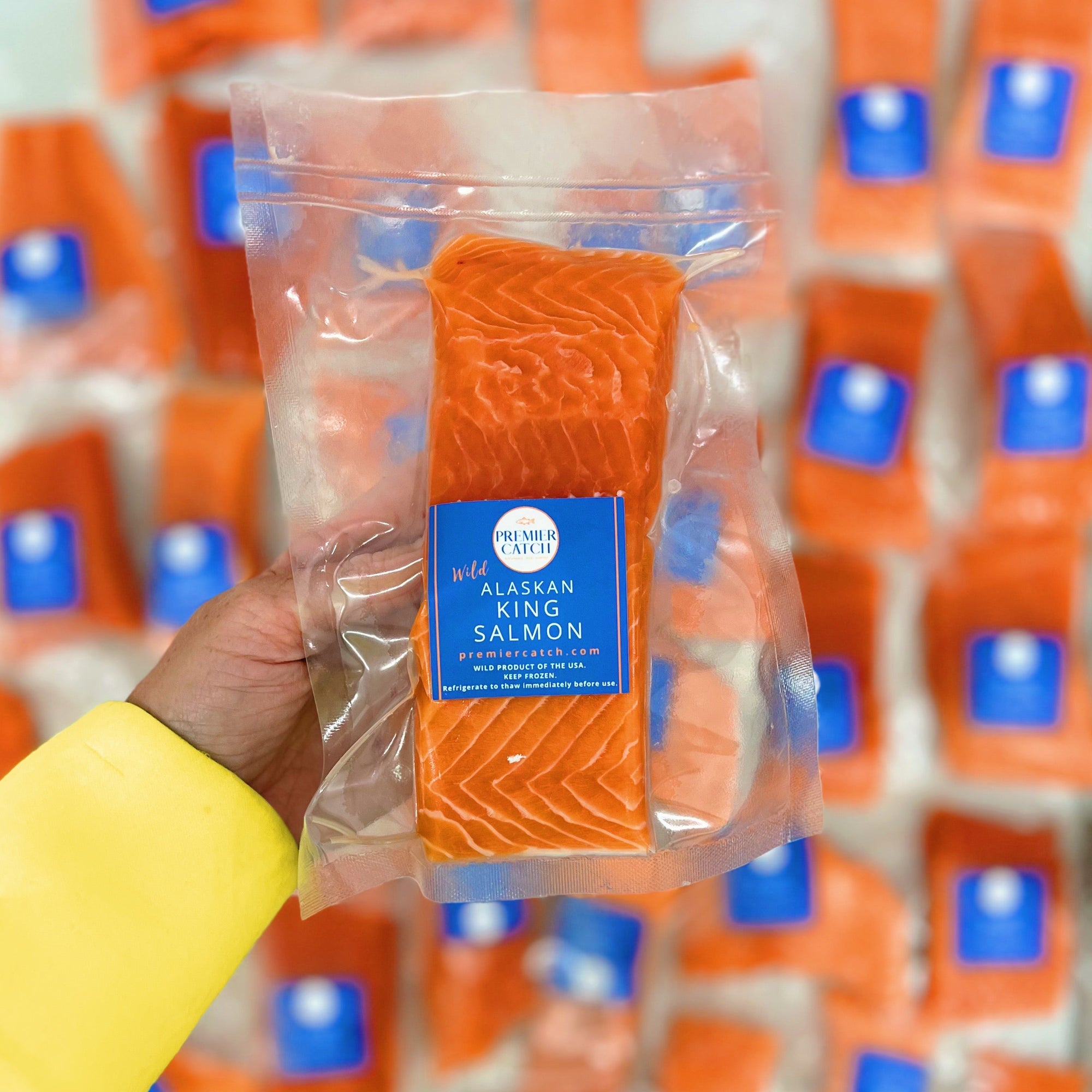 Packaged salmon fillet held by a hand with a blurred background of similar packaging.