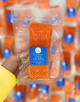 Packaged salmon fillet held by a hand with a blurred background of similar packaging.