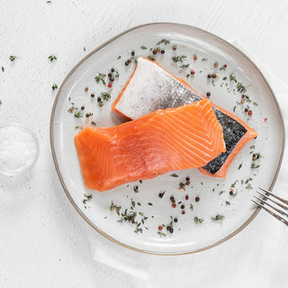 Two pieces of salmon on a plate with herbs and spices, on a light background.