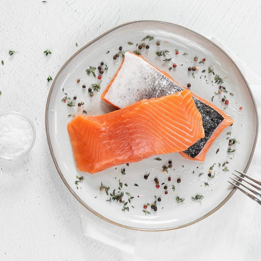 Two pieces of salmon on a plate with herbs and spices, on a light background.