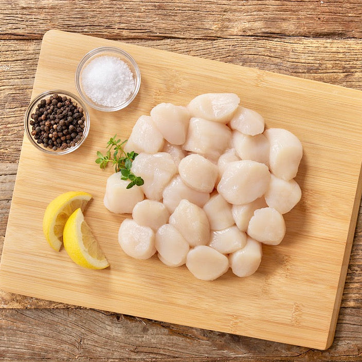Wild Alaska weathervane scallops arranged on a wooden cutting board with lemon