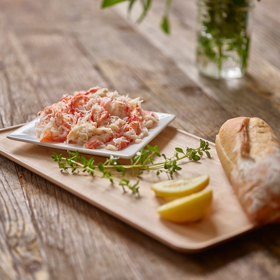 Wild snow crab meat on a plate with lemon wedge and fresh bread on a rustic table