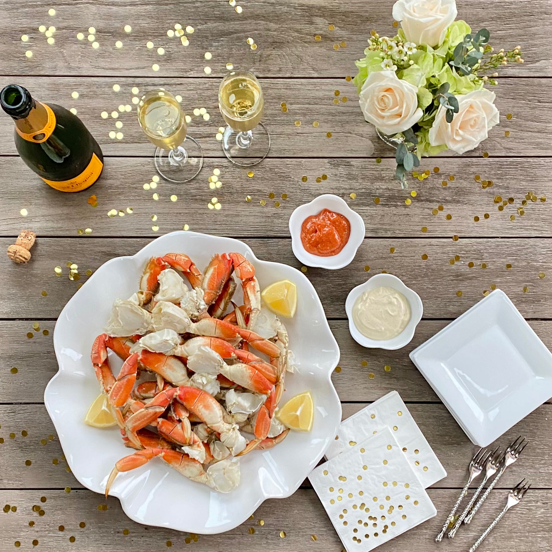 Wild caught Dungeness crab displayed on a fancy plate at a holiday dinner party with champagne, lemons, sauce, and crab forks on Christmas, Hanukkah, or New Year's Eve.