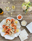 Wild caught Dungeness crab displayed on a fancy plate at a holiday dinner party with champagne, lemons, sauce, and crab forks on Christmas, Hanukkah, or New Year's Eve.