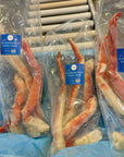 Packaged Alaskan Red King Crab legs with blue labels on a refrigerated shelf.