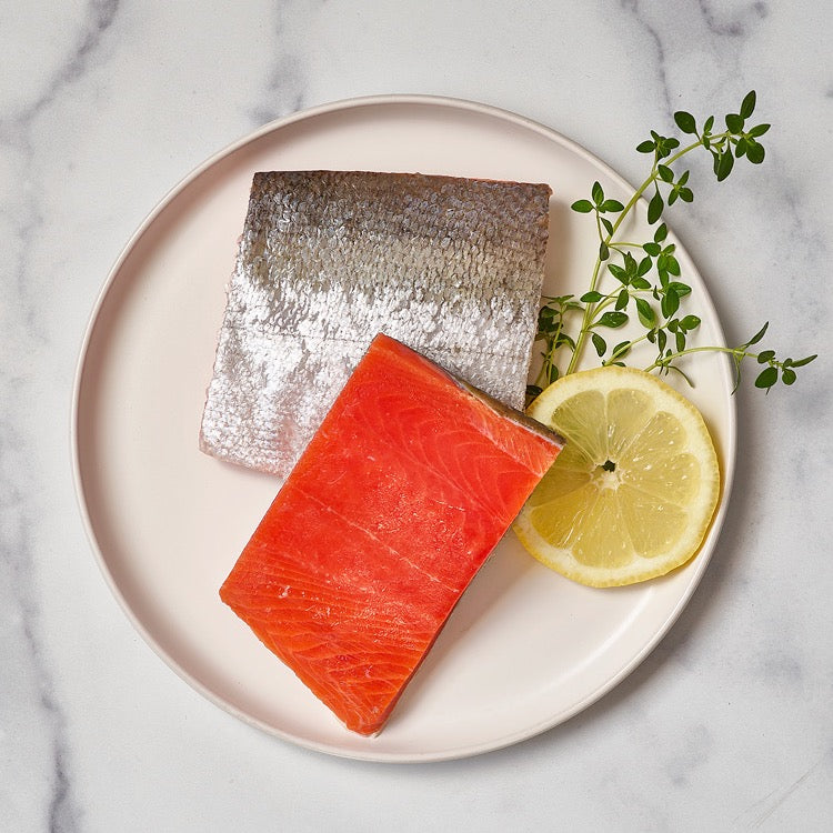Wild Alaskan sockeye salmon portions on a plate with lemon and herbs.