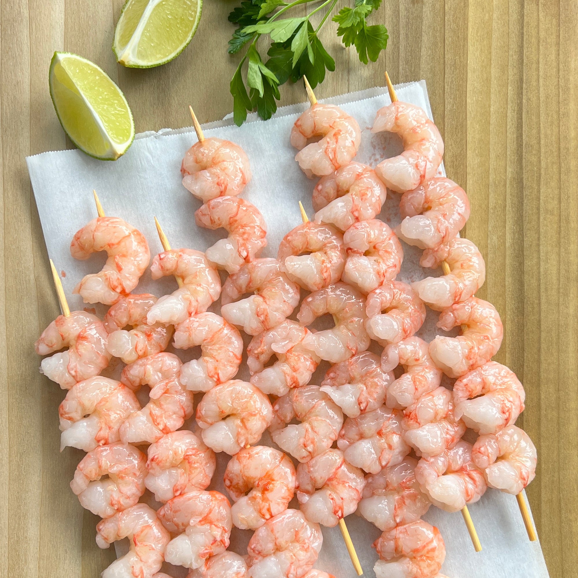 Raw wild Alaskan spot prawn skewers on a tray with lime wedges