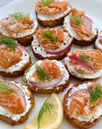 Smoked salmon crostini with cream cheese, onions, and dill on a white plate.