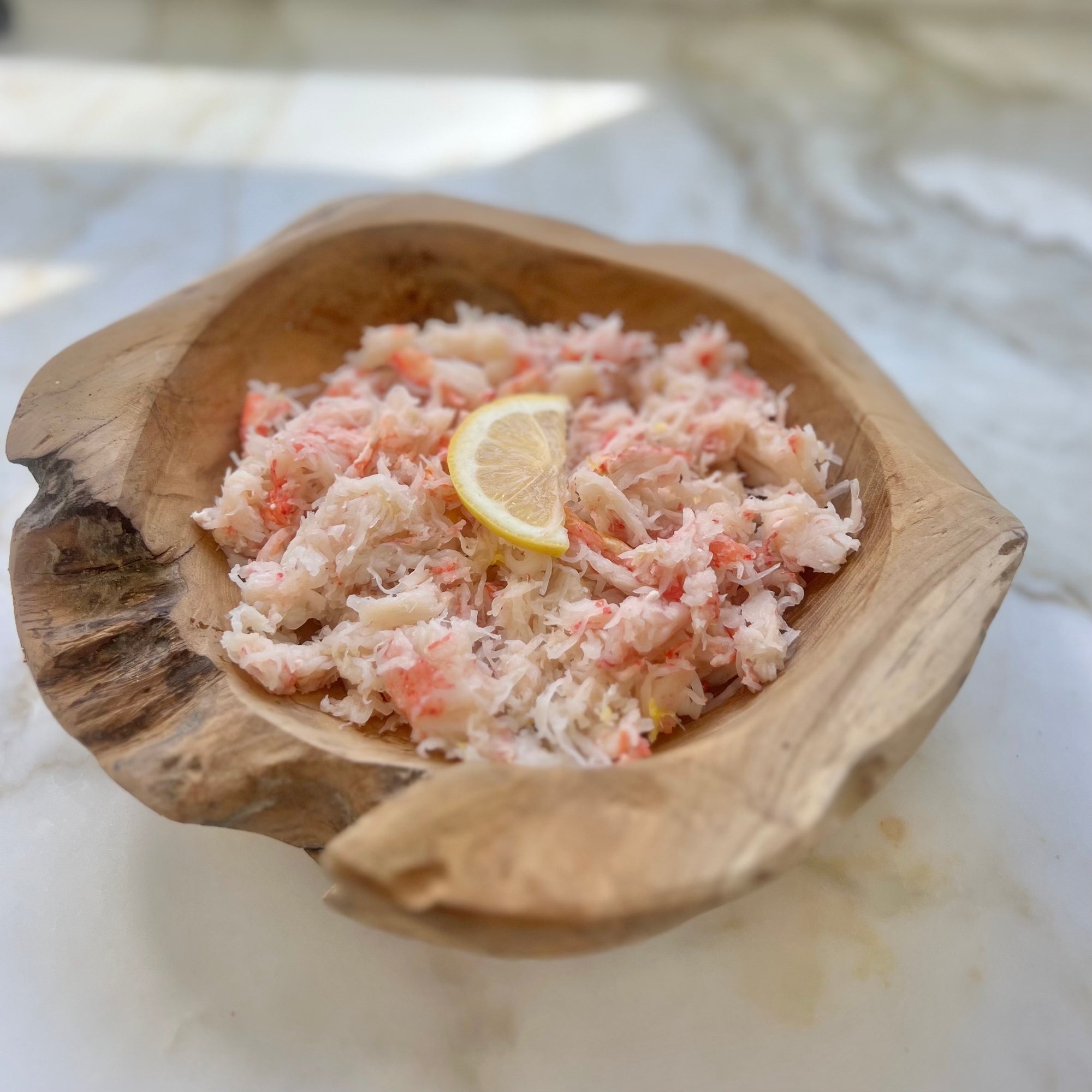 Wild snow crab meat in a wooden bowl with a lemon wedge