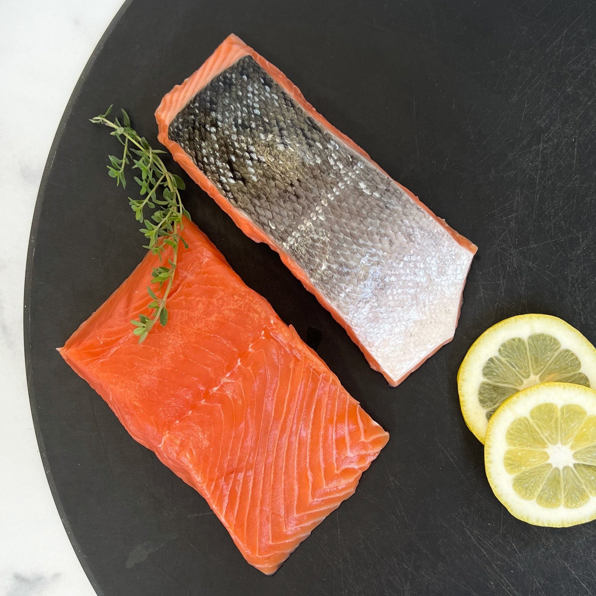 Two wild king salmon portions on black board with lemon slices